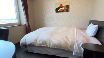 Habitación de hotel con cama, una mesita, una silla, una ventana con cortinas y un cuadro decorativo en la pared.