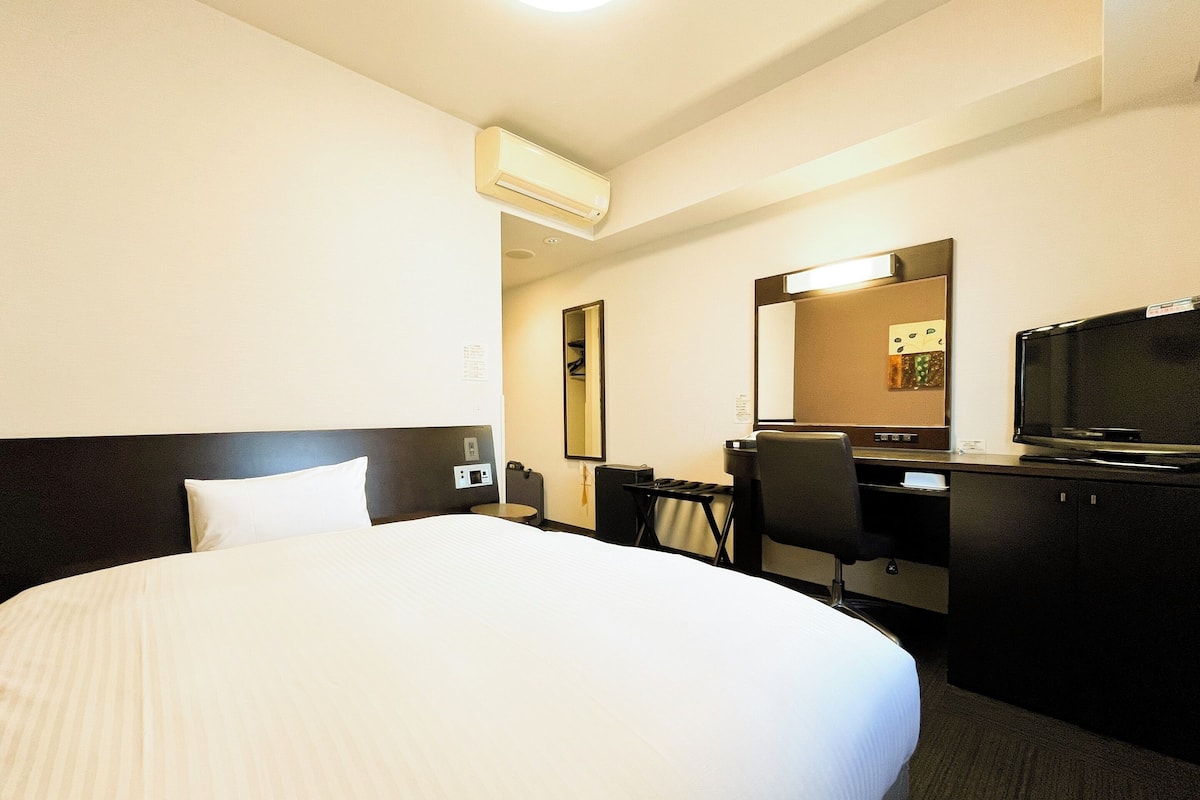 Una habitación de hotel con una cama grande, un escritorio con silla, un televisor y un equipo de aire acondicionado.