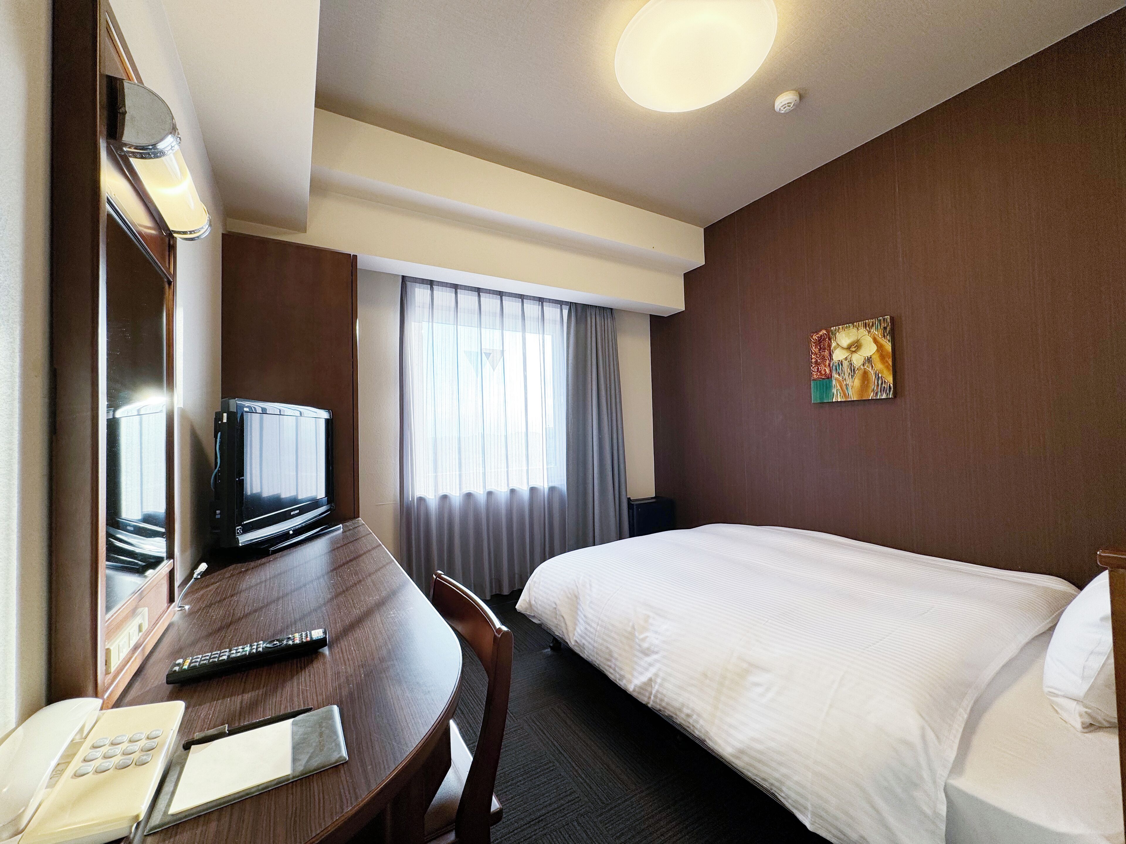 A hotel room with a bed, a desk with a television, a telephone, and a painting on the wall.