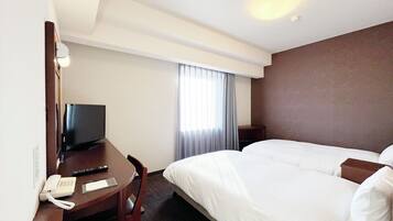 Una habitación de hotel con una cama, un escritorio con teléfono, una televisión y una ventana con cortinas.