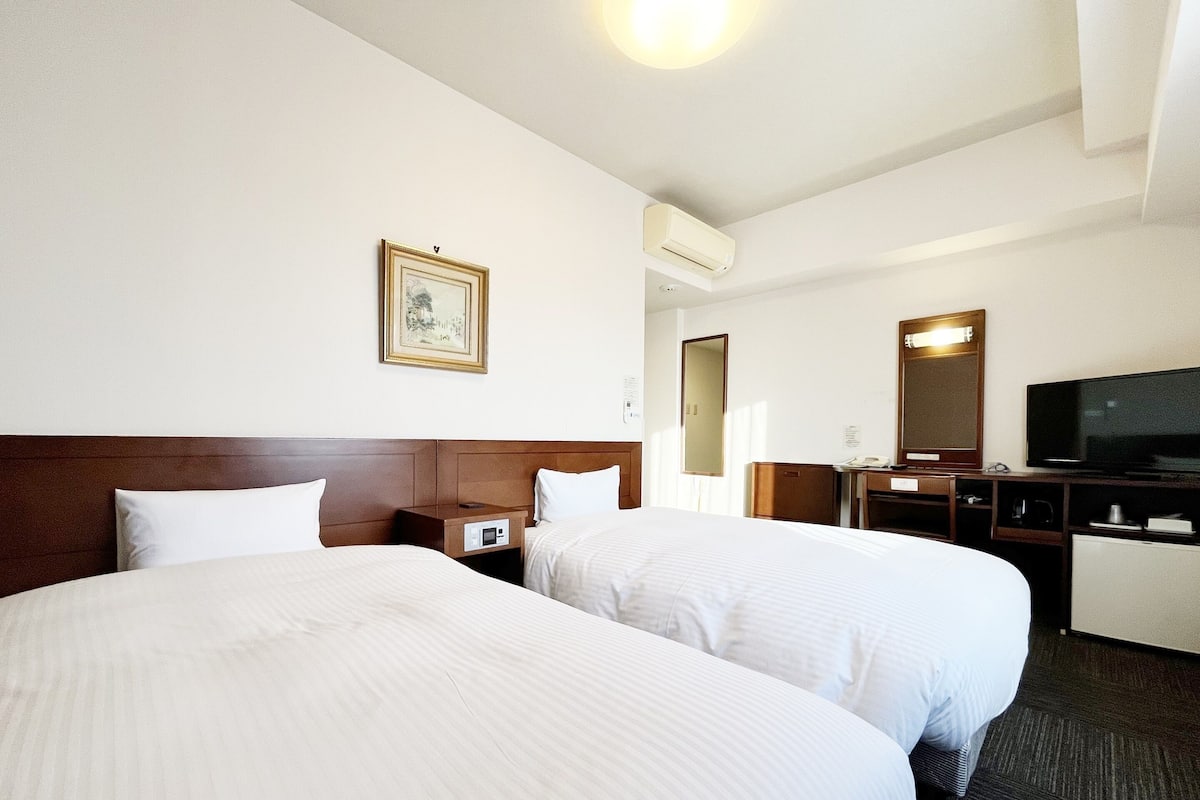 Una habitación de hotel con dos camas, un escritorio, un televisor y un espejo.