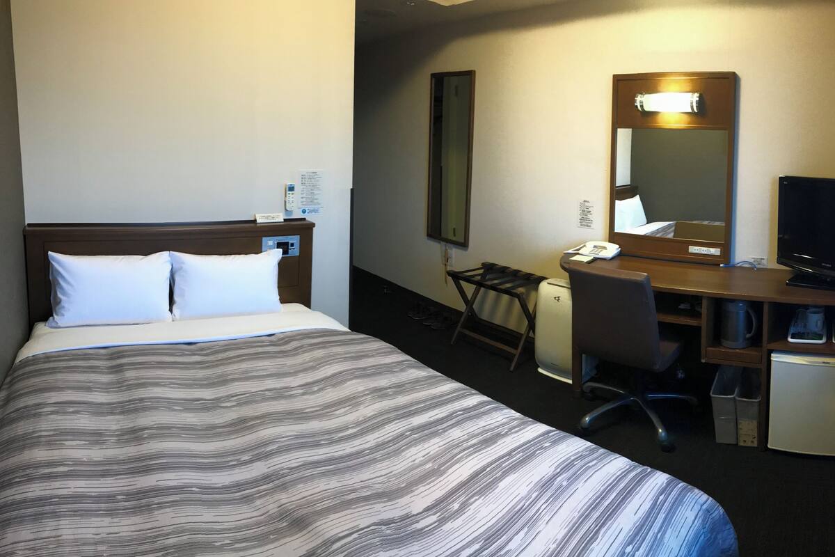 A hotel room with a bed, desk, chair, television, and a small refrigerator.