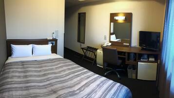 Una habitación de hotel con cama, escritorio, silla, televisión y un refrigerador pequeño.