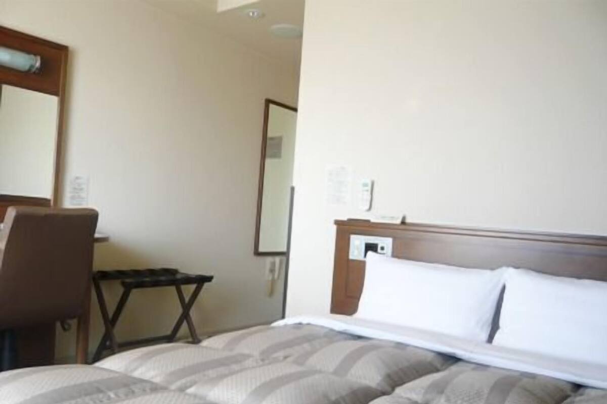 A hotel room with a bed, a chair, a small table, and a mirror on the wall.