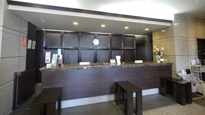 A reception area with a dark wood reception desk, two wooden benches, a clock, and a flower arrangement. - Hotel Route-Inn Koriyama Inter (Koriyama)