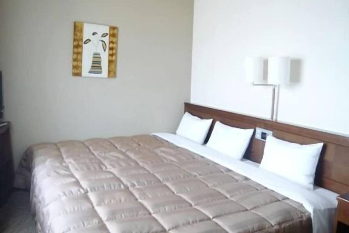 A hotel room with a large bed, a wooden headboard, two bedside lamps, and a wall-mounted artwork.