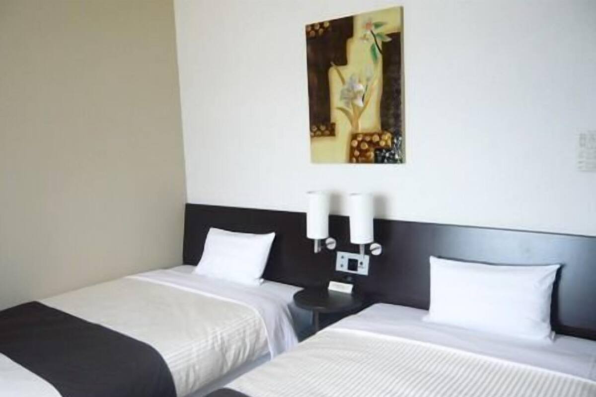 A hotel room with two beds, a nightstand, and a wall-mounted light fixture.