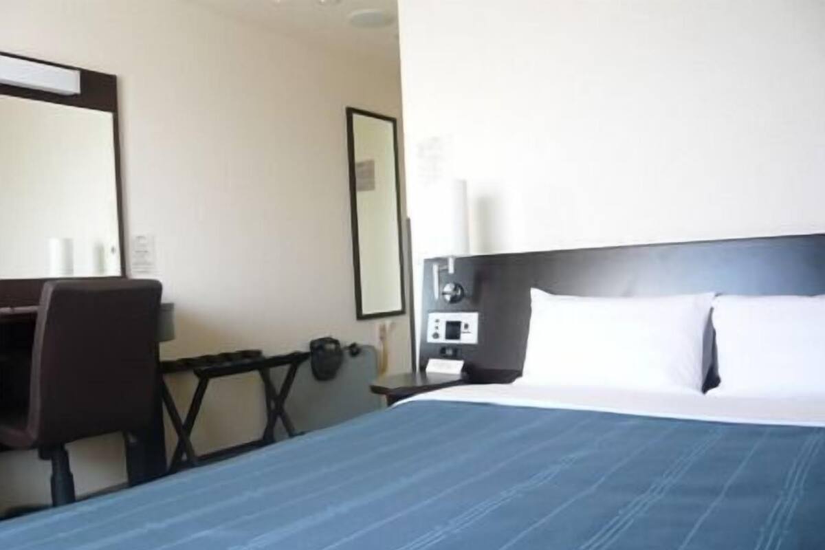 A hotel room with a large bed, a desk, a chair, a nightstand, and a mirror.