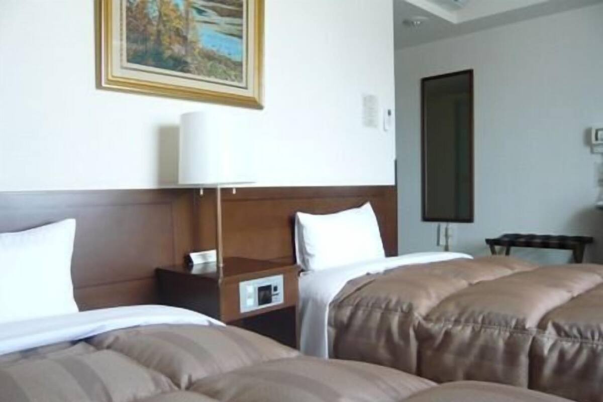 A hotel room with two beds, a nightstand, a lamp, and a painting on the wall.