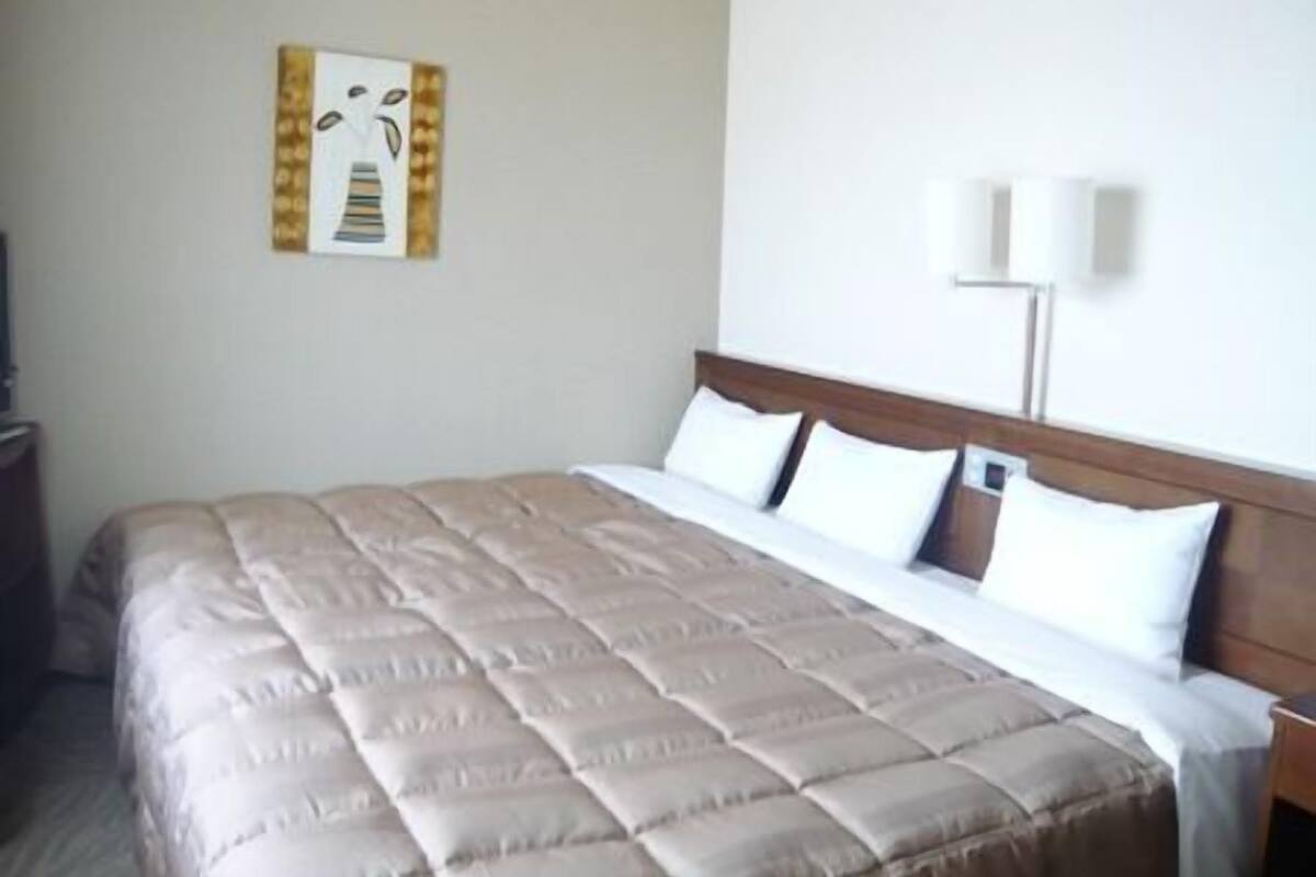 A hotel room with a large bed, a nightstand, a wall-mounted lamp, and a framed picture.