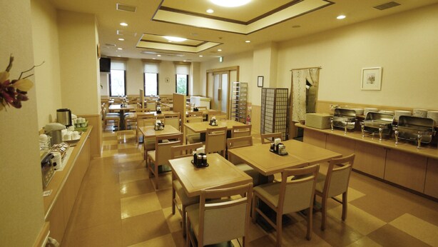 A hotel dining area with multiple tables and chairs, a buffet counter with trays, and a ceiling with recessed lighting. - Hotel Route Inn Tsubamesanjo Ekimae (Sanjo)
