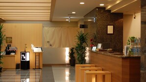 A hotel reception area with a wooden reception desk, a digital information kiosk, potted plants, and a tiled floor. - Route Inn Grantia Himi Wakuranoyado (Himi)