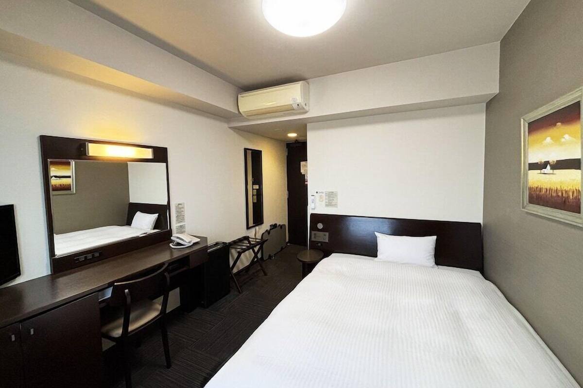 A hotel room with a bed, desk, chair, and a large mirror.