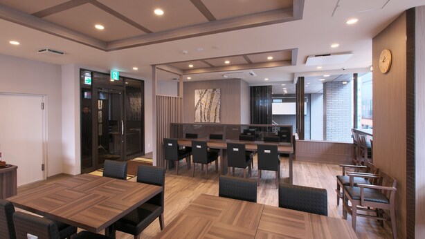 A modern hotel lobby with a wooden reception desk, seating area, and a view of the cityscape. - Hotel Route Inn Toyama Ekimae (Toyama)