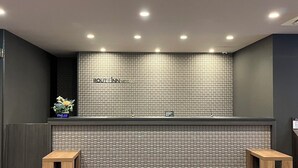 A reception desk with a tiled wall, a digital clock, and two wooden stools. - Hotel Route Inn Toyama Ekimae (Toyama)