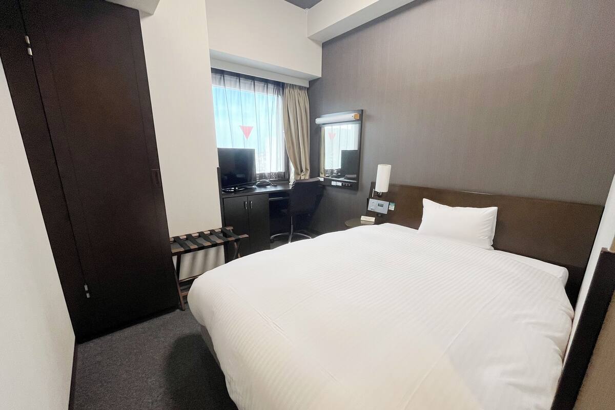 A hotel room with a large bed, a desk with a computer, a TV, and a mirror.