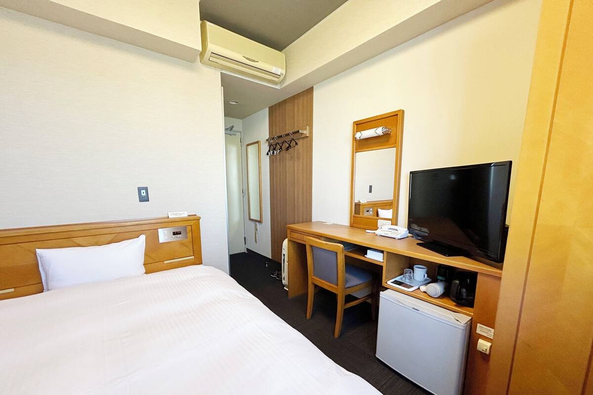 A hotel room with a bed, a desk with a computer, a television, and a mini-fridge.