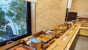 Un espace buffet proposant une variété de plats, notamment du bacon, des oignons frits et d’autres mets, présentés sur un comptoir avec un mur de briques en arrière-plan.
