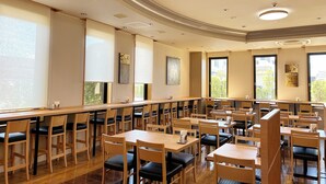 Une salle de conférence spacieuse, dotée de longues tables et de chaises, de grandes fenêtres et de luminaires au plafond.