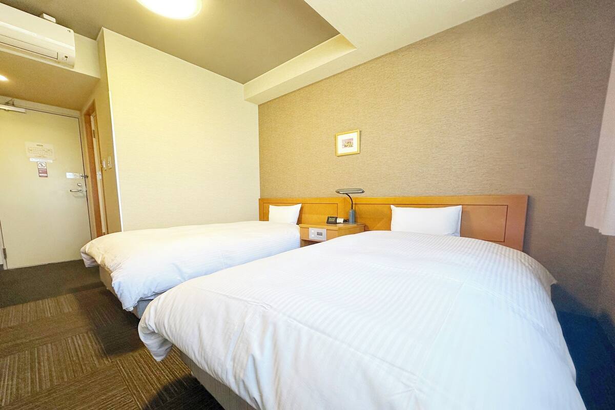 A hotel room with two beds, a wooden headboard, a nightstand with a lamp, and a wall-mounted picture.