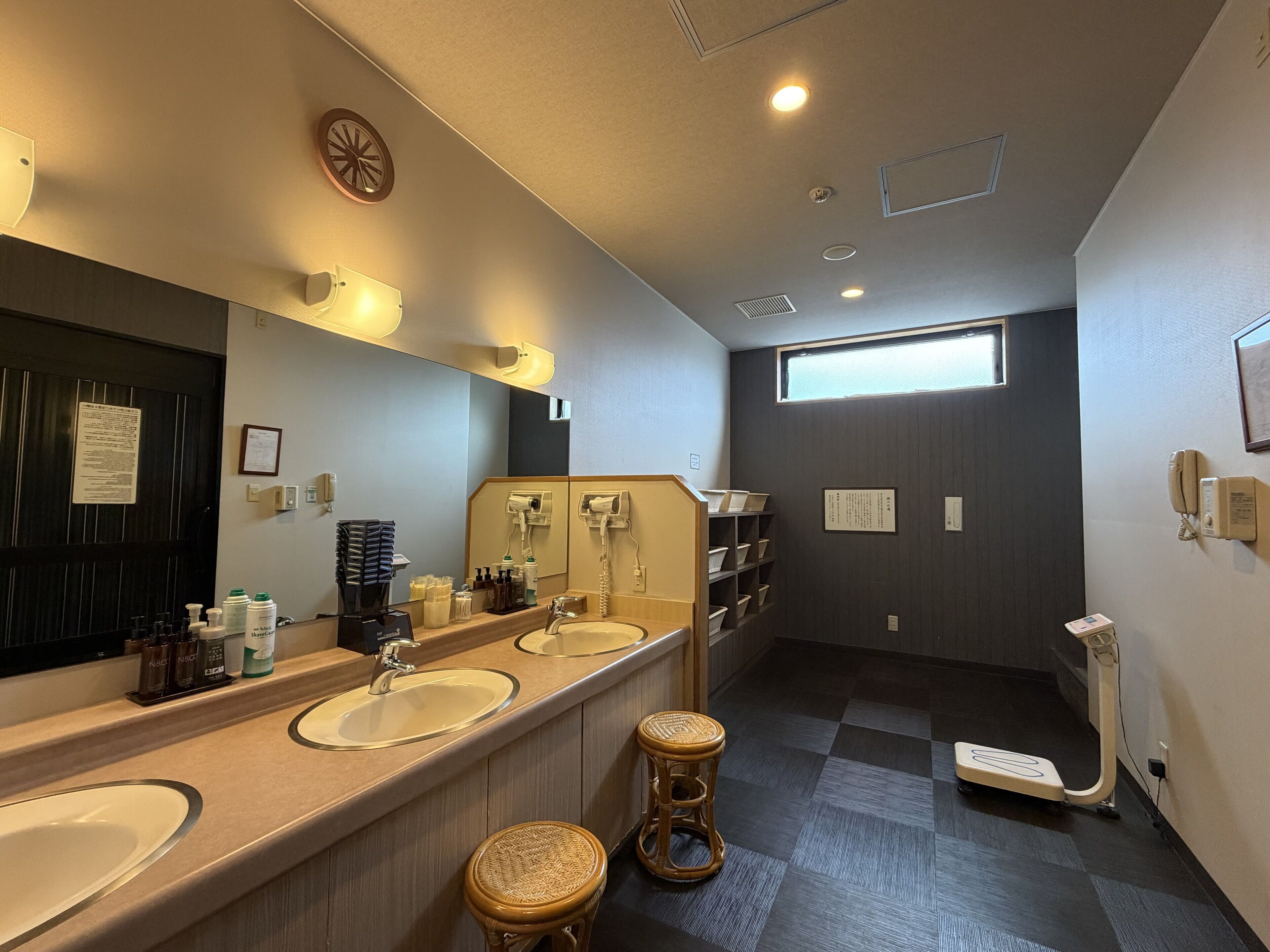 A hotel bathroom with two sinks, a large mirror, a window, and a toilet with a bidet attachment.
