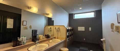 A hotel bathroom with two sinks, a large mirror, a window, and a toilet with a bidet attachment.
