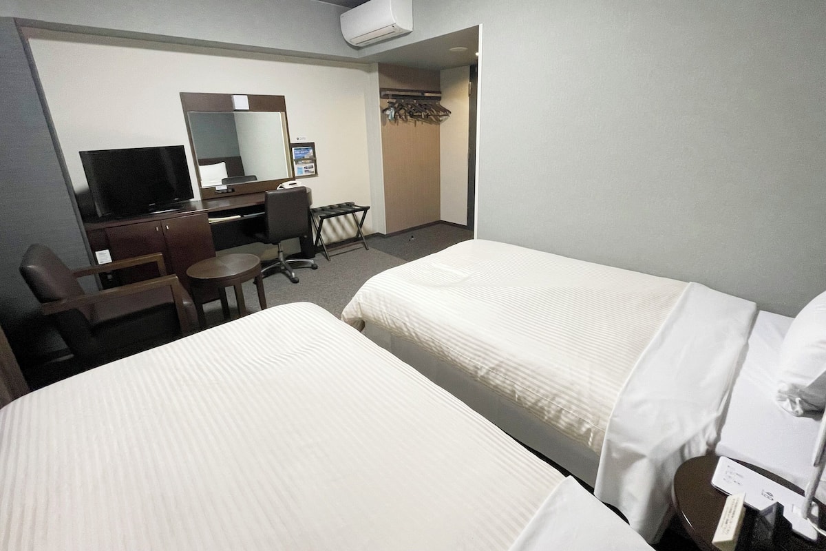 Habitación de hotel con dos camas, un escritorio con computadora, televisión y aire acondicionado.