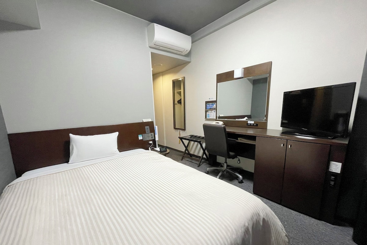 Habitación de hotel con una cama grande, un escritorio con silla, televisión y aire acondicionado.