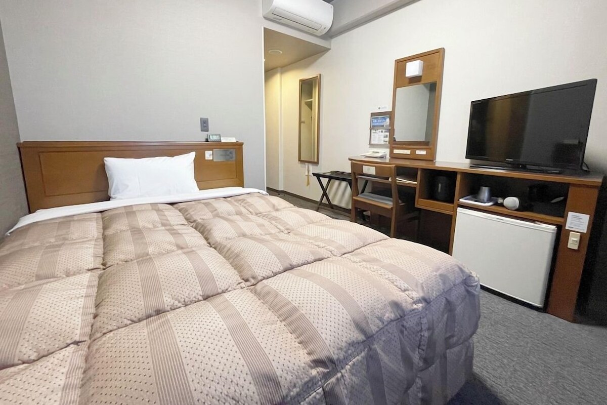 A hotel room with a bed, a desk, a television, and an air conditioning unit.