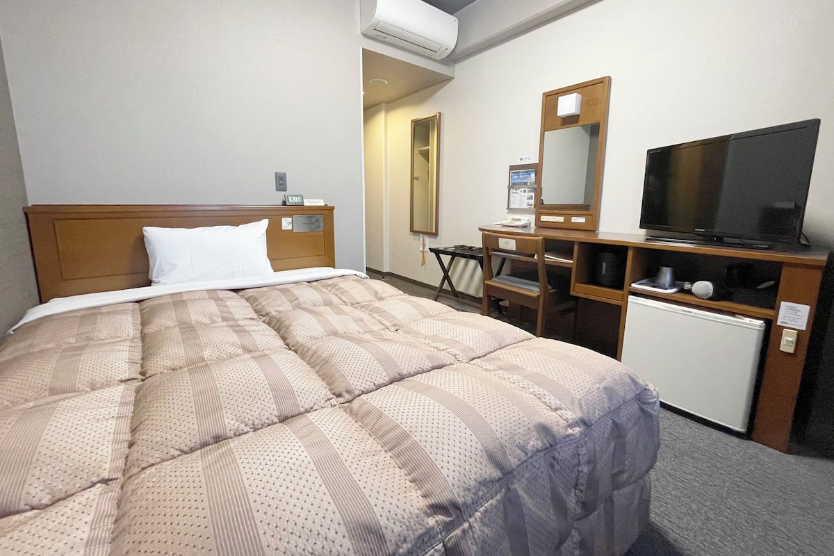 Habitación de hotel con cama, escritorio, televisión y refrigerador pequeño.