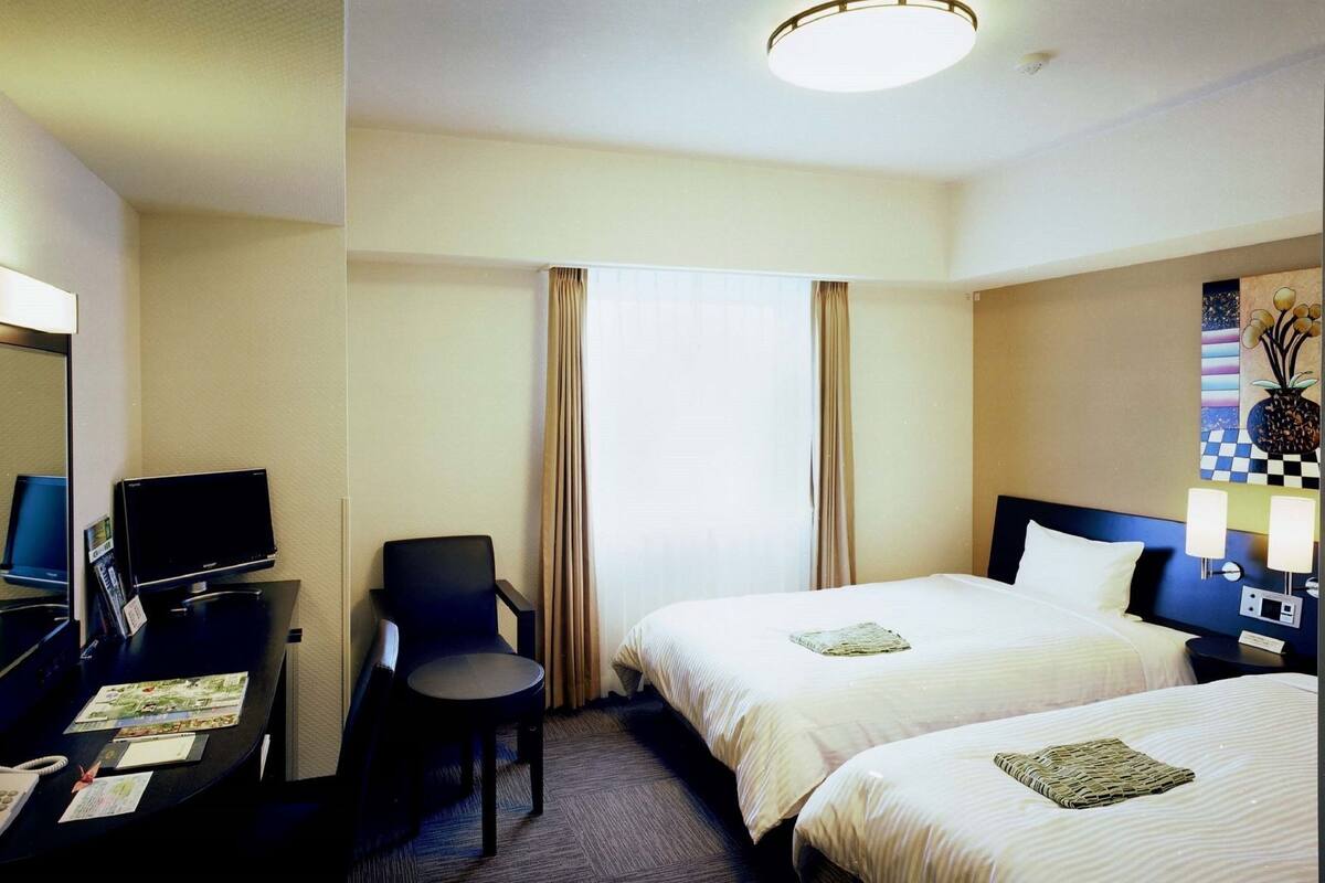 Habitación de hotel con dos camas, un escritorio con computadora, una silla y un televisor.