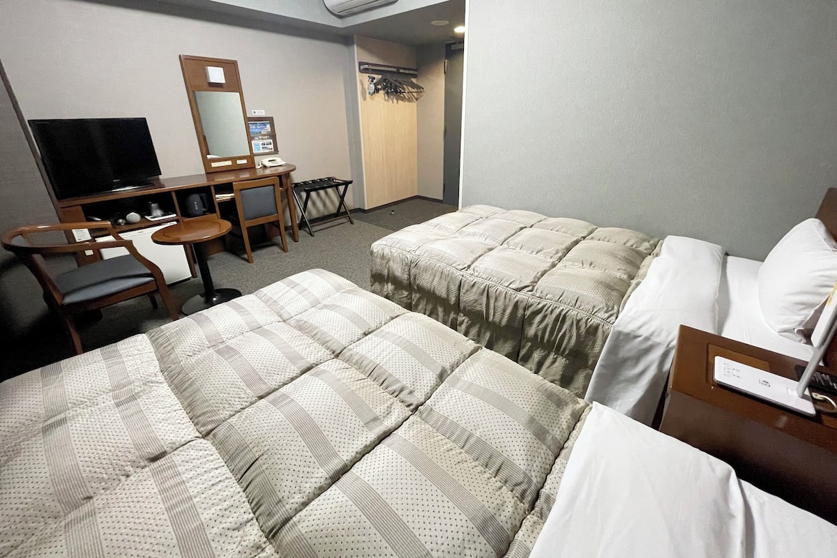 Habitación de hotel con dos camas, un escritorio con silla, televisor y espejo.