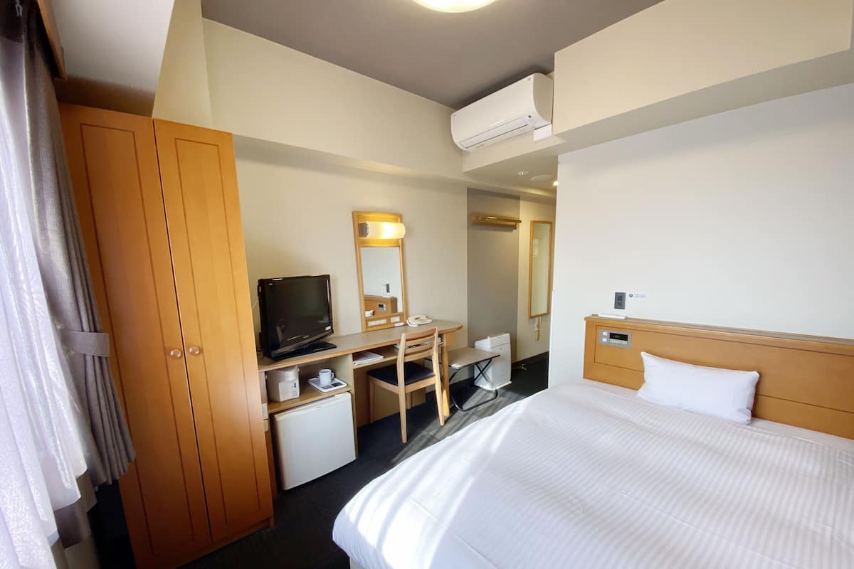 Ett hotellrum med en säng, ett skrivbord med en dator, en tv, en garderob och en luftkonditioneringsanläggning.