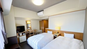 Habitación de hotel con dos camas, un escritorio con silla, televisor, lámpara de escritorio y espejo.