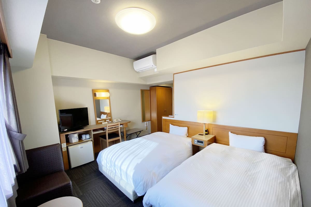 Ett hotellrum med två sängar, ett skrivbord med en stol, en tv, en skrivbordslampa och en spegel.