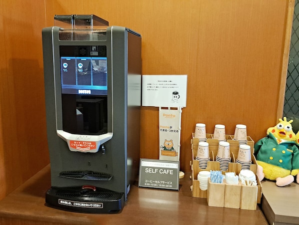Una máquina expendedora de café con pantalla digital, dispensador de tazas y un letrero para el café de autoservicio.
