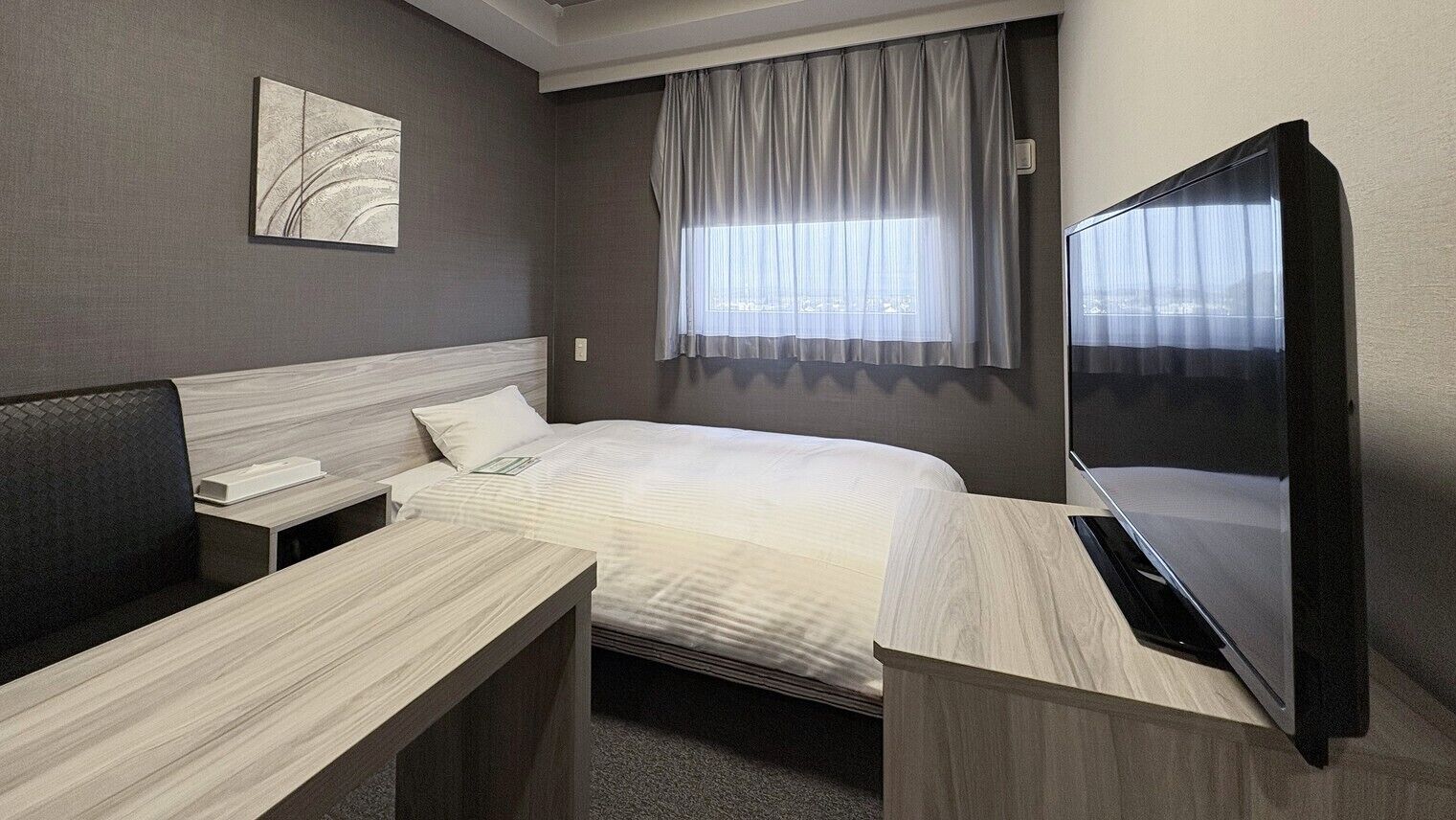 Ein Hotelzimmer mit einem Bett, einem Schreibtisch, einem Stuhl, einem Fernseher und einem Fenster mit Vorhängen.