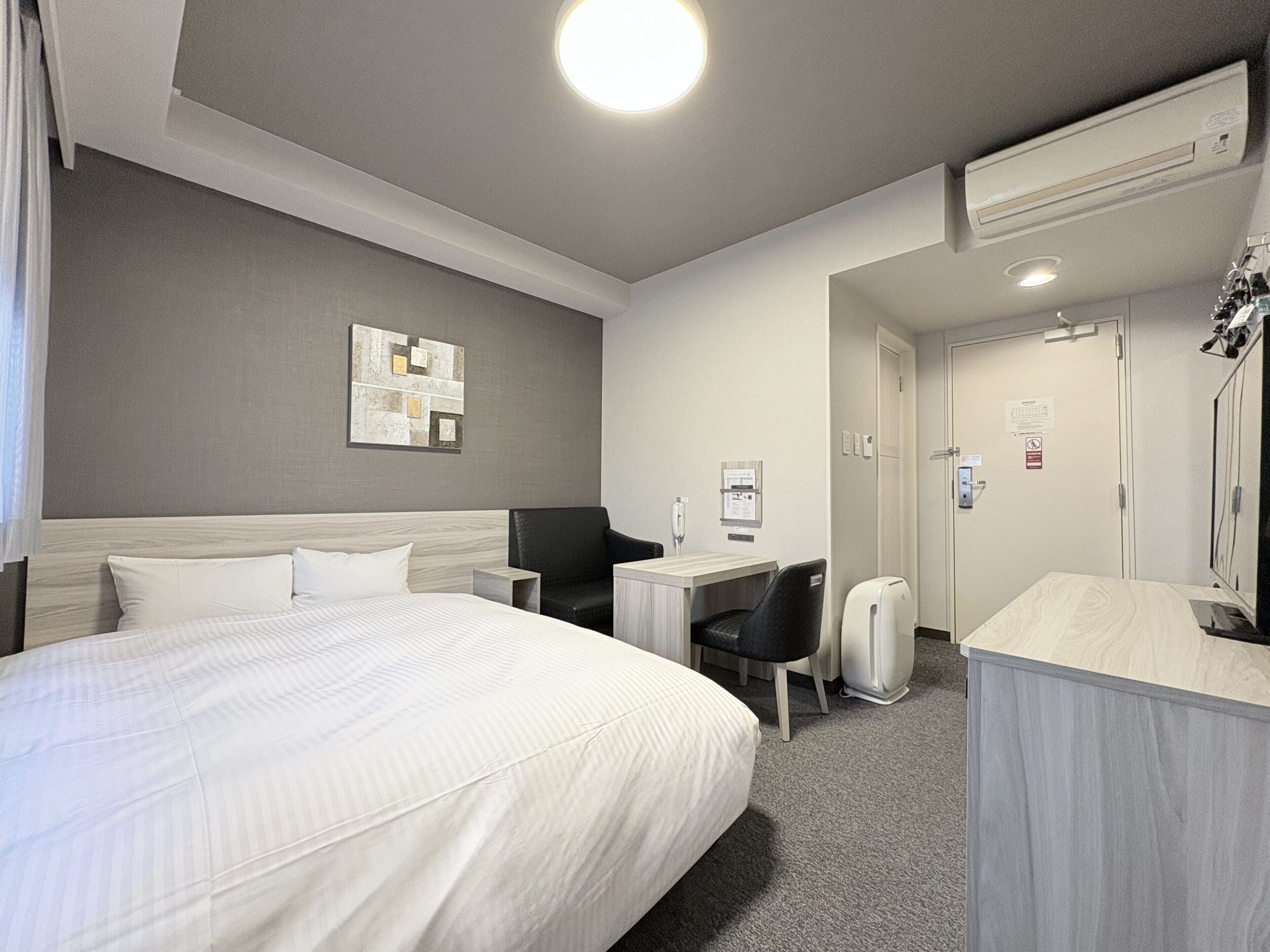 Ein Hotelzimmer mit einem großen Bett, einem Schreibtisch, einem Stuhl, einem Kleiderschrank und einem Spiegel.