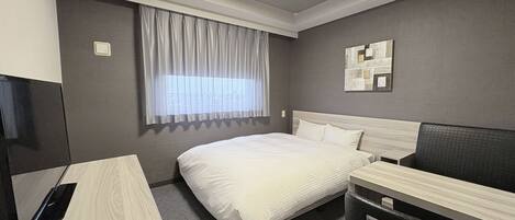A hotel room with a bed, a desk, a chair, a window with curtains, a wall-mounted artwork, and a ceiling light.