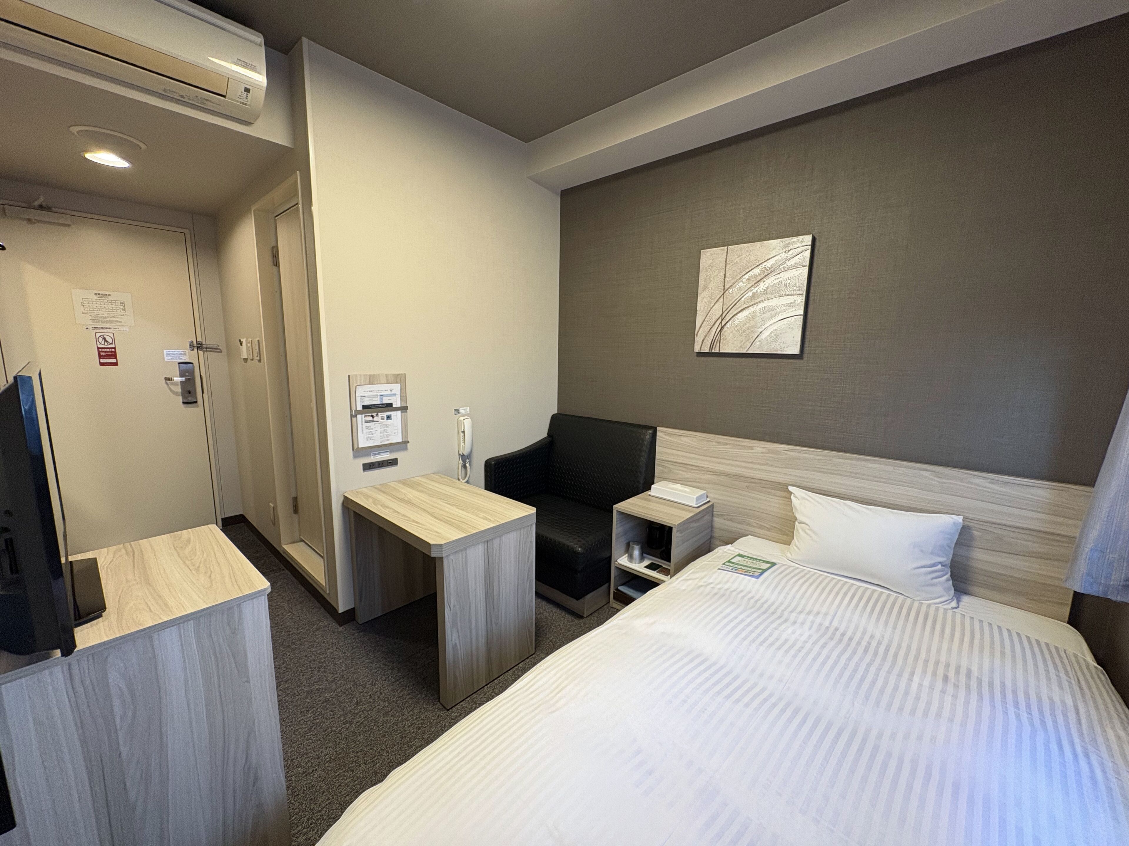 Ein Hotelzimmer mit einem Bett, einem Schreibtisch, einem Sessel, einem Nachttisch, einem Telefon und einem Wandbild.