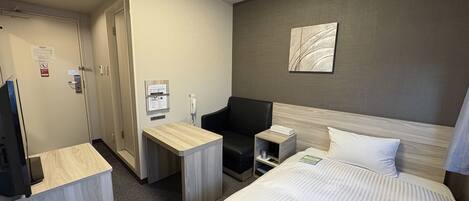Ein Hotelzimmer mit einem Bett, einem Schreibtisch, einem Sessel, einem Nachttisch, einem Telefon und einem Wandbild.