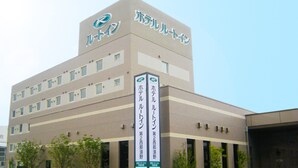 A multi-story building with a prominent logo at the top. There are several windows on the facade, and a sign with Japanese text is visible on the side.
