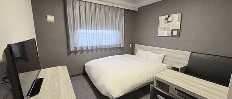 A hotel room with a bed, a desk, a chair, a TV, a window with curtains, and a wall-mounted artwork.