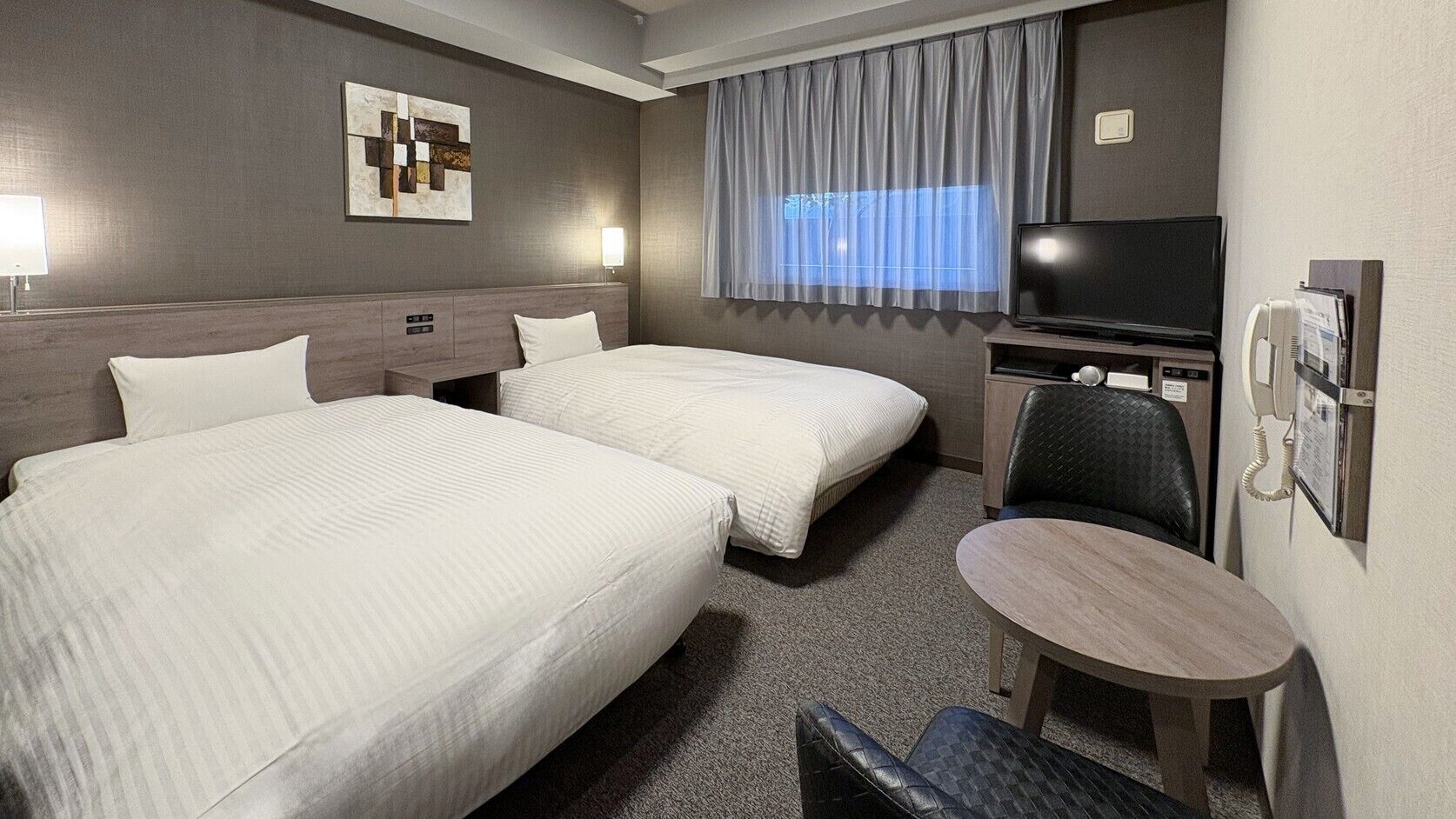 Ein Hotelzimmer mit zwei Betten, einem Fernseher, einem Schreibtisch und einem Stuhl.