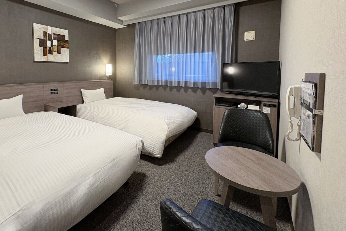 A hotel room with two beds, a TV, a desk, and a chair.