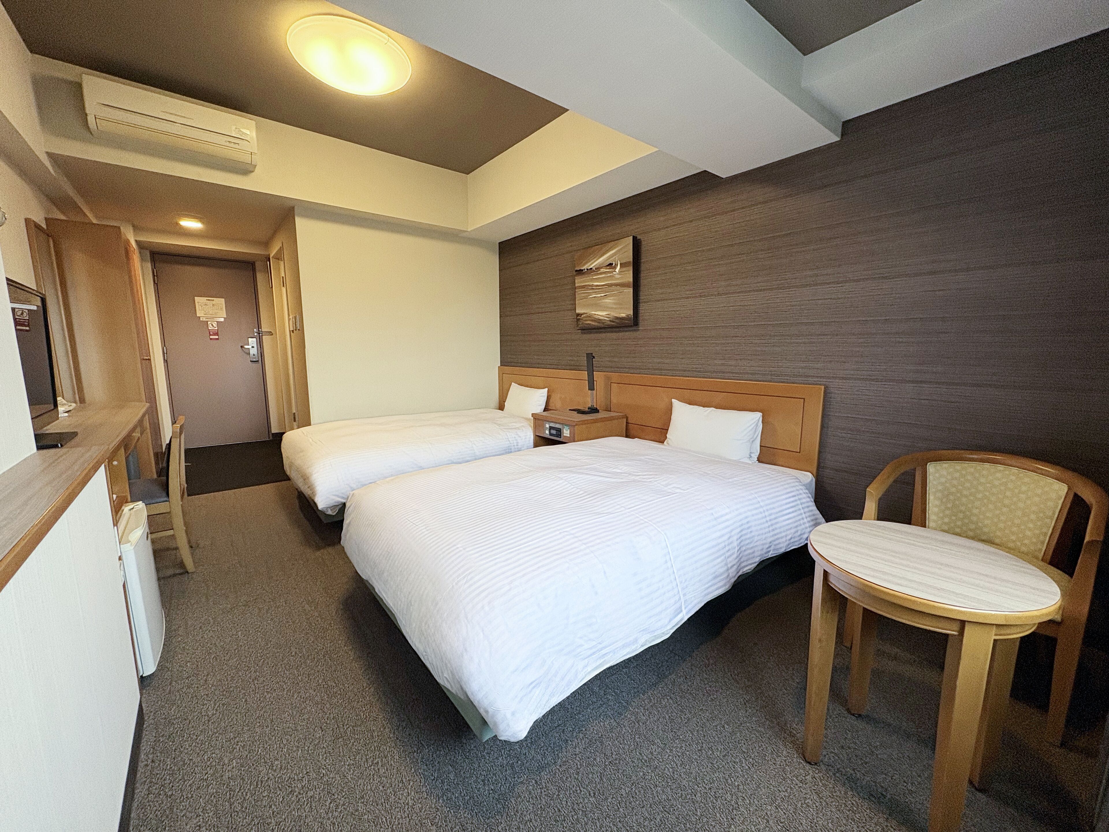 Ein Hotelzimmer mit zwei Betten, einem Schreibtisch, einem Stuhl und einer Wand-Klimaanlage.