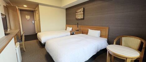 Ein Hotelzimmer mit zwei Betten, einem Schreibtisch, einem Stuhl und einer Wand-Klimaanlage.