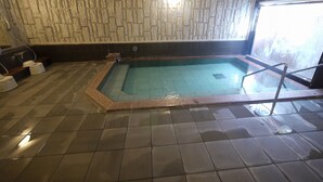 A swimming pool with a stone wall backdrop, a tiled floor, and a window on the right. - Hotel Route - Inn Nishinasuno (Nasushiobara)
