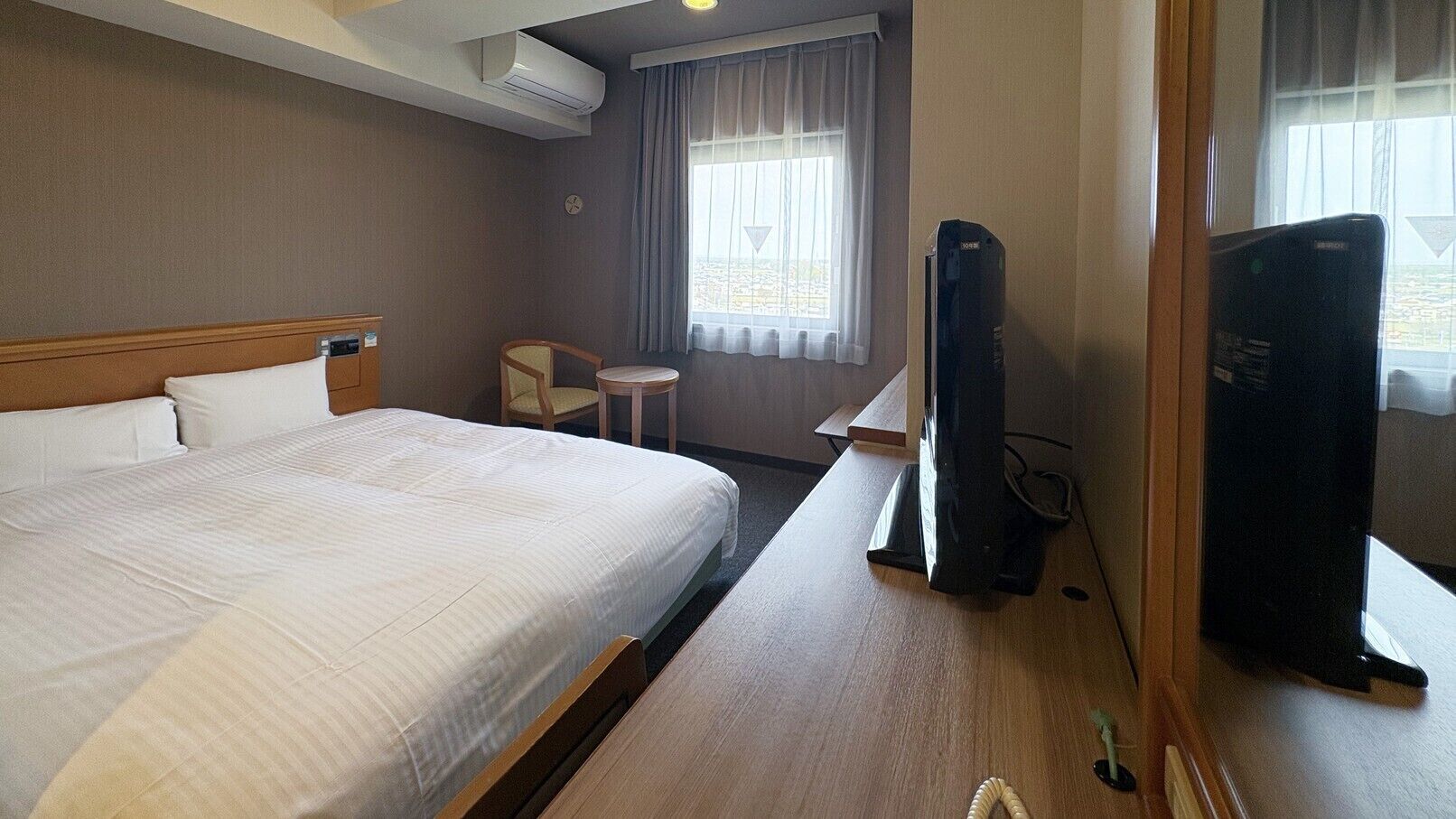 A hotel room with a bed, a desk, a chair, a TV, and a window with curtains.
