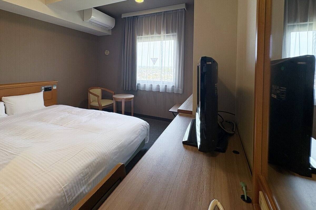 A hotel room with a bed, a desk, a chair, a TV, and a window with curtains.